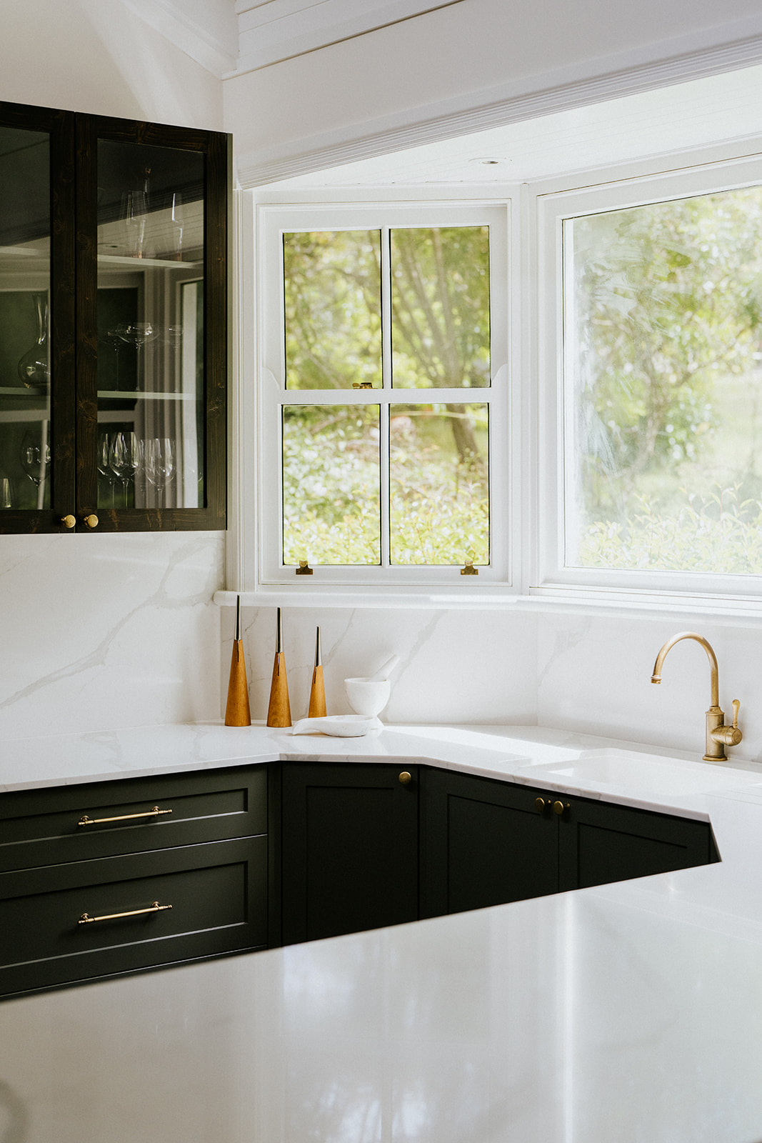 Dark kitchen — black cabinetry, marble benchtop, brass tapware, garden outlook
