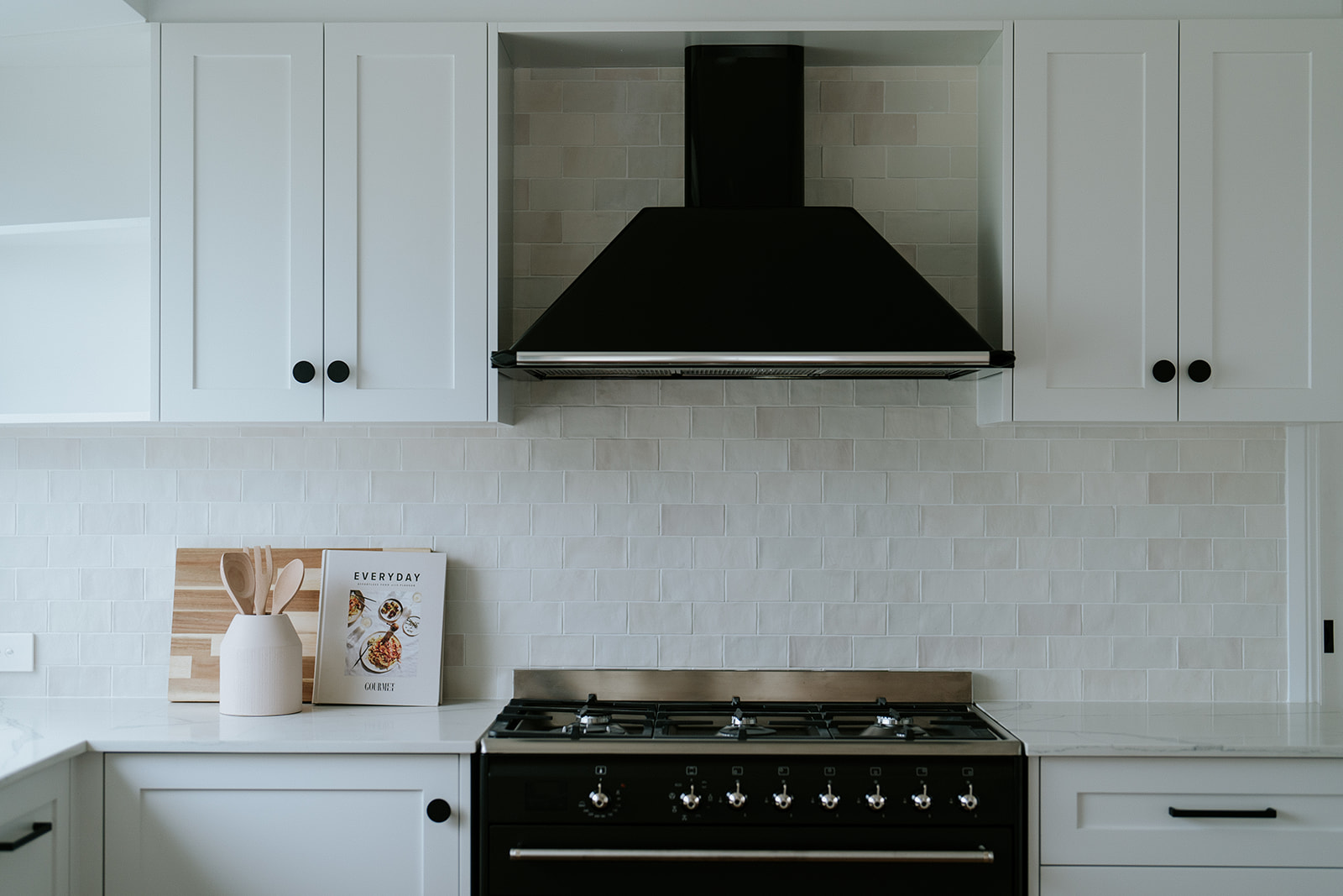 White shaker kitchen with black rangehood, subway tile splashback, gas cooktop